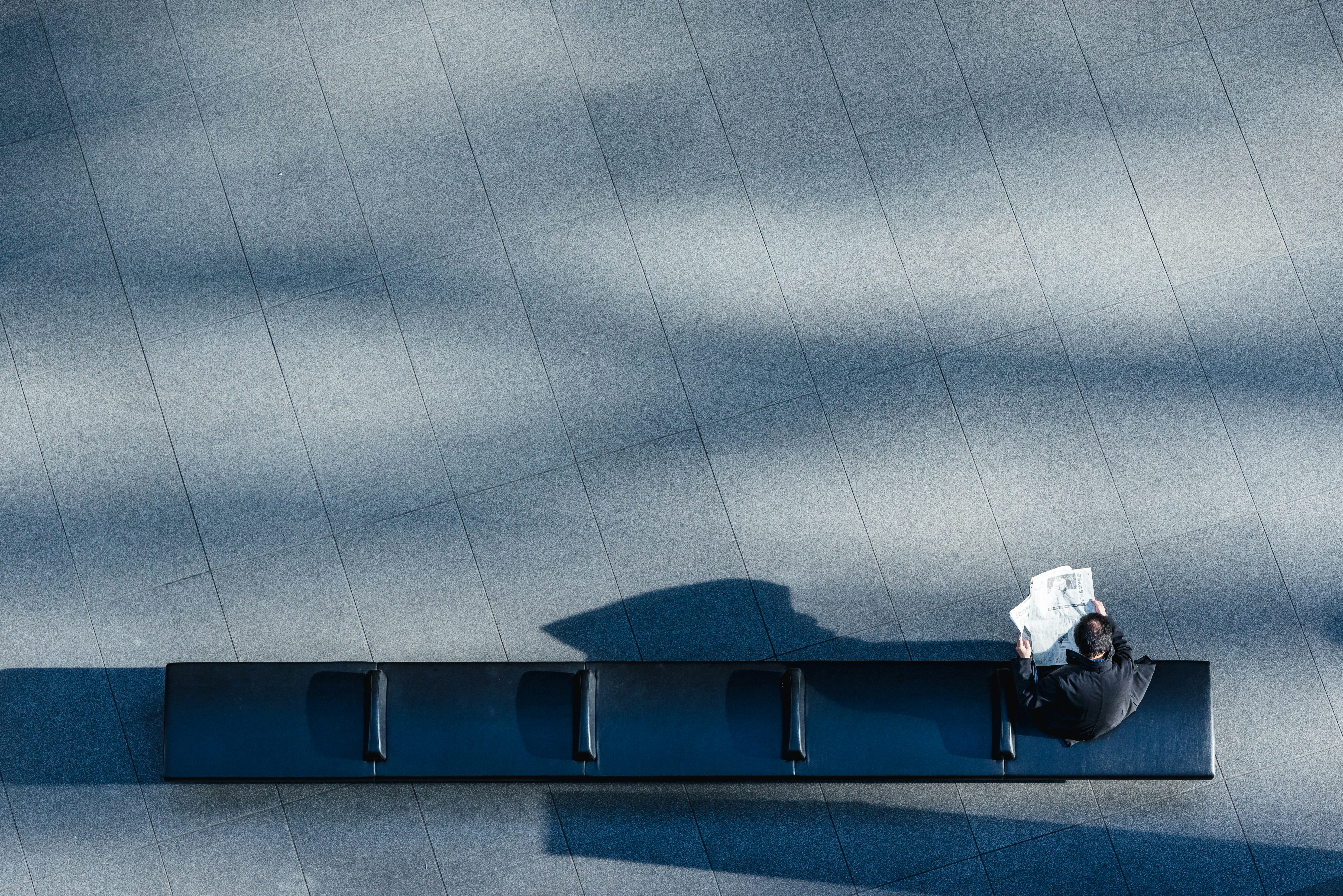Businessman sitting alone on a bench in a modern urban space reading a newspaper, symbolising business decisions and responsibility.